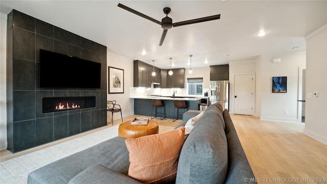 living room with a tile fireplace, sink, ceiling fan, ornamental molding, and light hardwood / wood-style floors