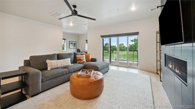 living room with ceiling fan, crown molding, a tile fireplace, and light hardwood / wood-style flooring