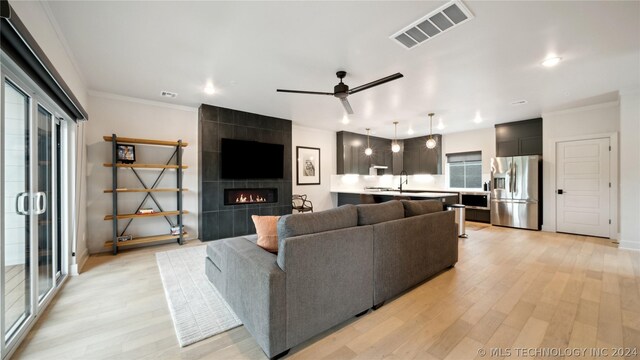 living room with a tile fireplace, light hardwood / wood-style flooring, ceiling fan, and ornamental molding