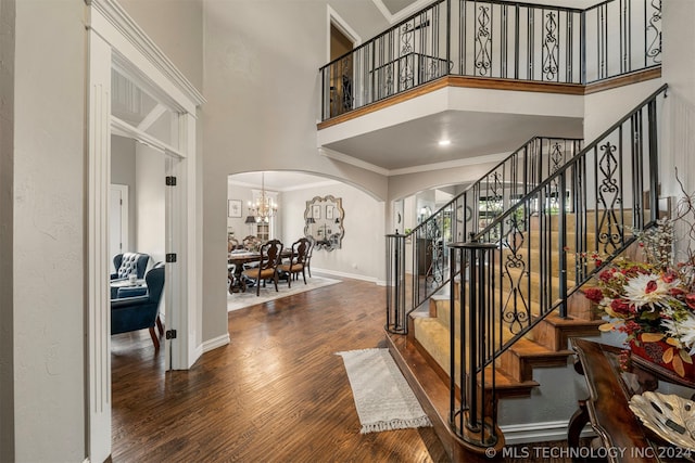 foyer entrance featuring an inviting chandelier, crown molding, dark wood-type flooring, and a high ceiling