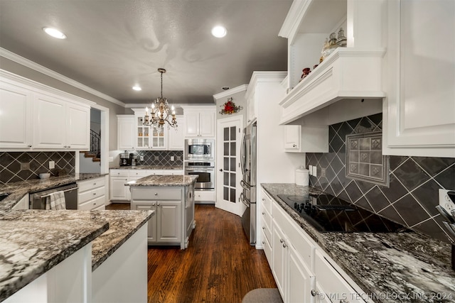 kitchen with white cabinets, appliances with stainless steel finishes, dark stone counters, dark wood-type flooring, and decorative light fixtures