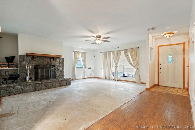 unfurnished living room with a stone fireplace, wood-type flooring, and ceiling fan