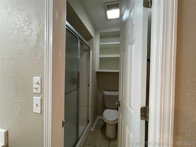 bathroom with tile patterned flooring, toilet, and a shower with door