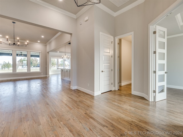 unfurnished living room featuring light hardwood / wood-style floors, ornamental molding, a towering ceiling, and an inviting chandelier