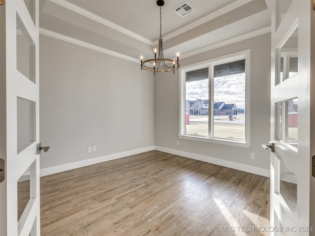 unfurnished room with a raised ceiling, ornamental molding, wood-type flooring, and a notable chandelier