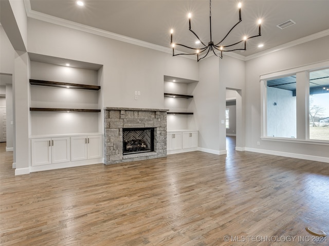 unfurnished living room with a stone fireplace, built in shelves, ornamental molding, and light wood-type flooring