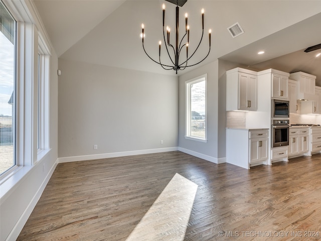 kitchen featuring backsplash, an inviting chandelier, vaulted ceiling, white cabinetry, and stainless steel appliances