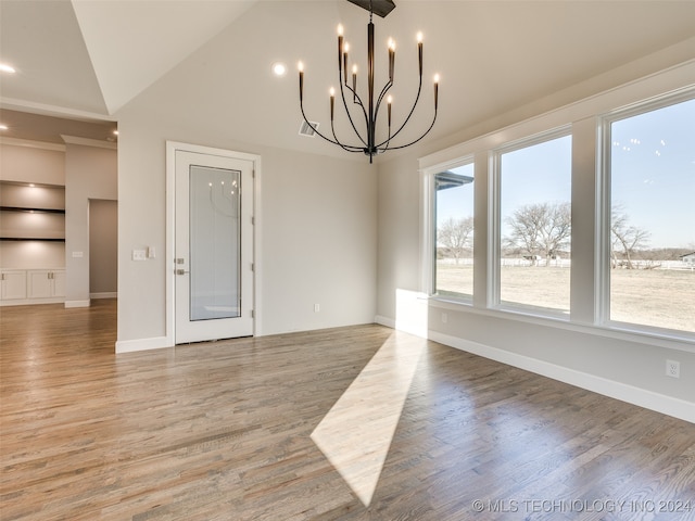 unfurnished dining area featuring built in features, wood-type flooring, an inviting chandelier, and vaulted ceiling