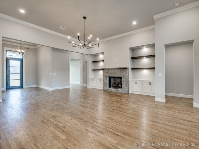 unfurnished living room featuring light hardwood / wood-style floors, a stone fireplace, ornamental molding, and an inviting chandelier