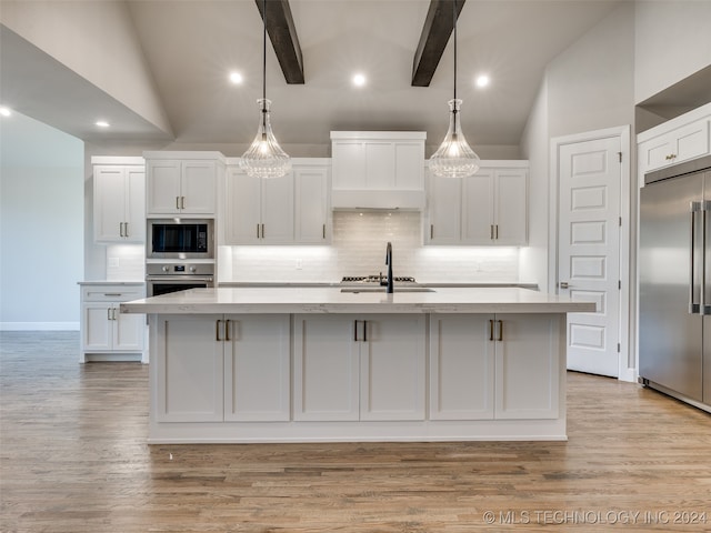 kitchen with built in appliances, white cabinetry, sink, and an island with sink