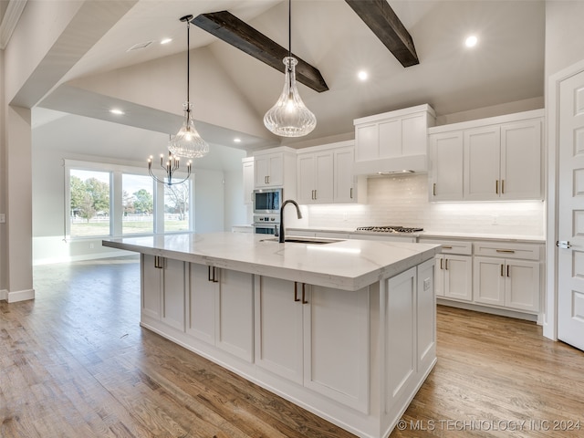 kitchen featuring beamed ceiling, white cabinetry, stainless steel appliances, and a large island with sink