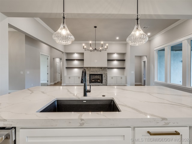 kitchen with a stone fireplace, light stone counters, sink, and decorative light fixtures