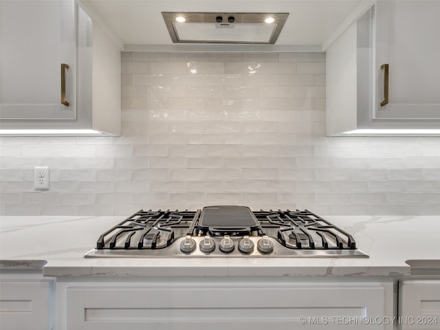 details with white cabinets, stainless steel gas stovetop, light stone counters, and tasteful backsplash