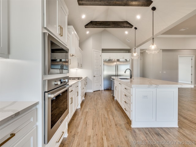 kitchen with a large island with sink, built in appliances, white cabinets, and sink