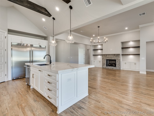 kitchen with a kitchen island with sink, sink, hanging light fixtures, built in shelves, and white cabinetry