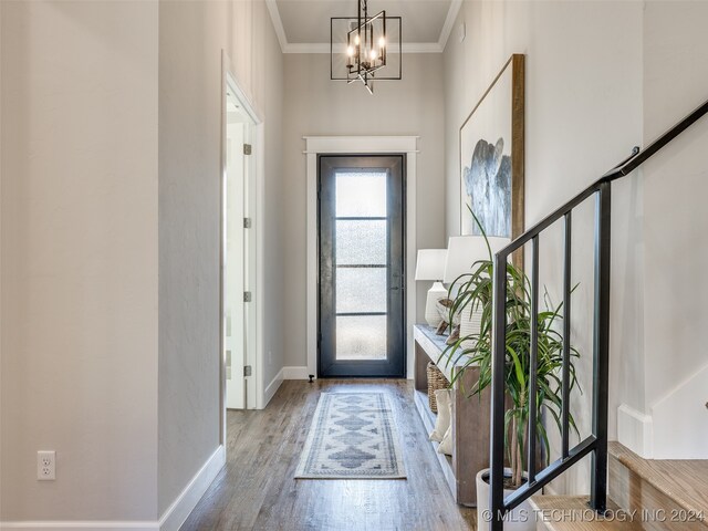 entryway with ornamental molding, wood-type flooring, and a notable chandelier