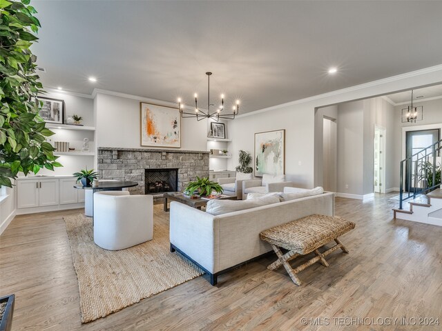 living room with light hardwood / wood-style floors, a stone fireplace, ornamental molding, and a notable chandelier