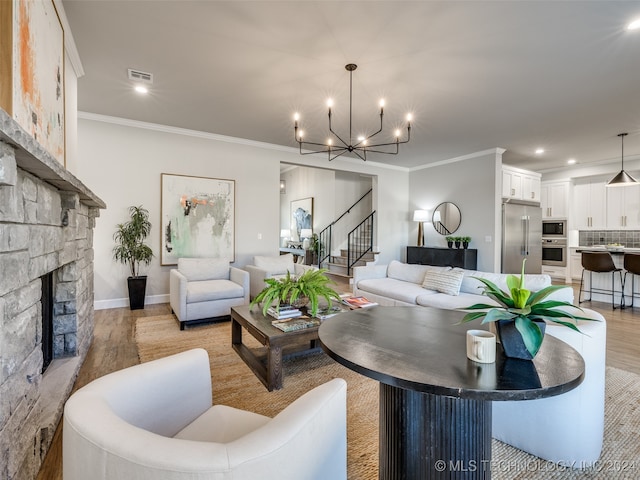 living room featuring crown molding, a fireplace, a notable chandelier, and light wood-type flooring