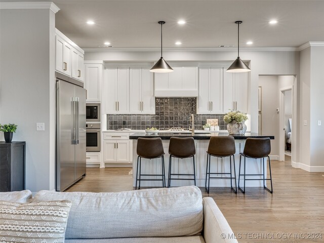 kitchen with a kitchen breakfast bar, decorative light fixtures, a center island with sink, white cabinets, and appliances with stainless steel finishes