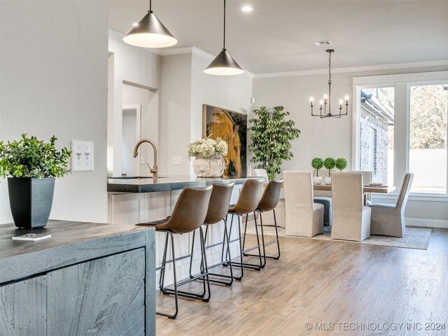 kitchen featuring a kitchen breakfast bar, pendant lighting, light hardwood / wood-style flooring, and crown molding