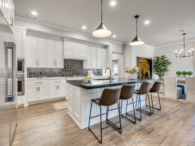 kitchen featuring white cabinets, a center island with sink, sink, light wood-type flooring, and decorative light fixtures