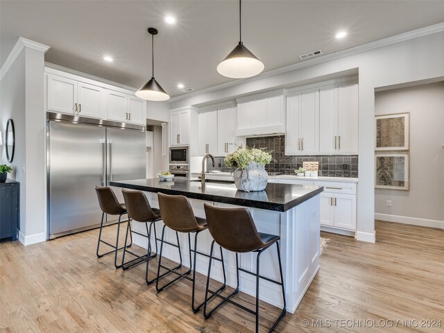 kitchen featuring built in appliances, light hardwood / wood-style flooring, white cabinetry, and an island with sink