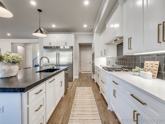 kitchen with white cabinetry, hanging light fixtures, stainless steel appliances, wood-type flooring, and ornamental molding