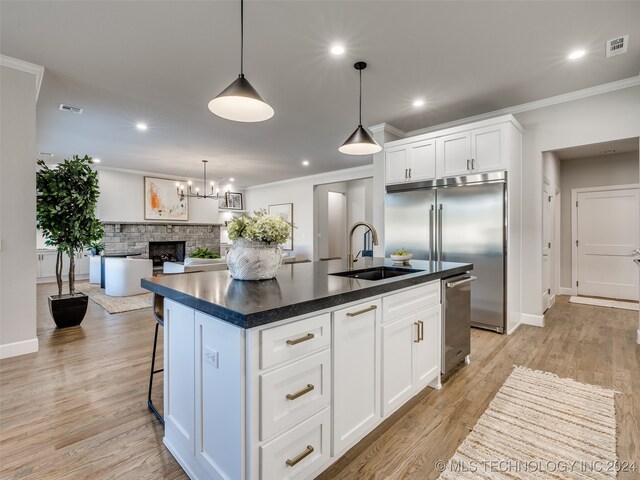 kitchen with light wood-type flooring, a fireplace, sink, a center island with sink, and white cabinets