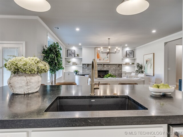 kitchen with pendant lighting, sink, ornamental molding, a fireplace, and a notable chandelier