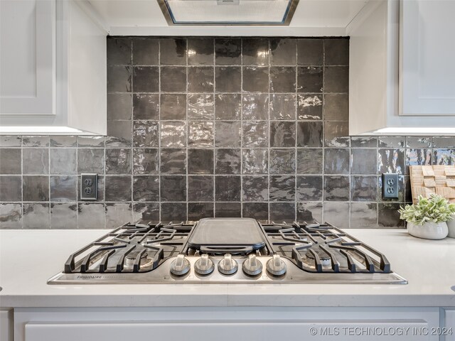 room details featuring white cabinets, decorative backsplash, ventilation hood, and stainless steel gas stovetop