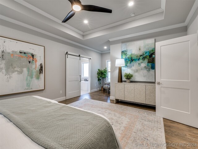 bedroom with ceiling fan, a barn door, wood-type flooring, and ornamental molding