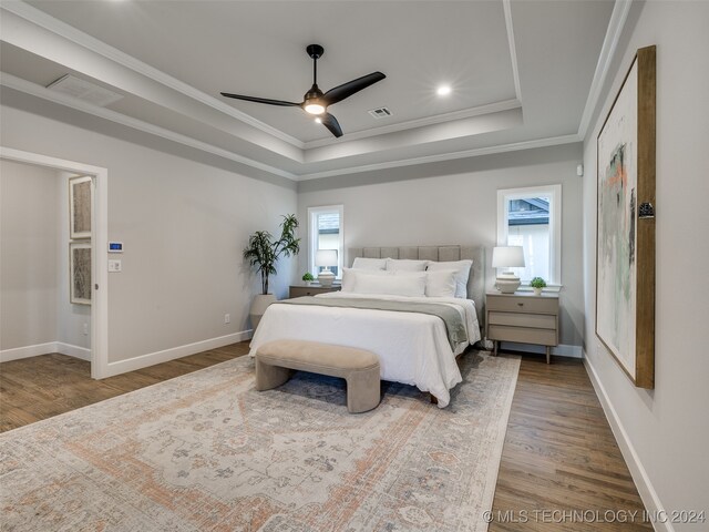 bedroom featuring hardwood / wood-style flooring, a raised ceiling, ceiling fan, and crown molding