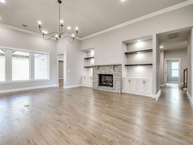 unfurnished living room featuring built in shelves, a healthy amount of sunlight, a stone fireplace, and light hardwood / wood-style floors