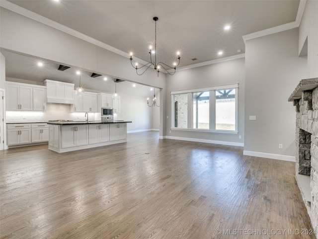 unfurnished living room with sink, an inviting chandelier, light hardwood / wood-style flooring, crown molding, and a fireplace