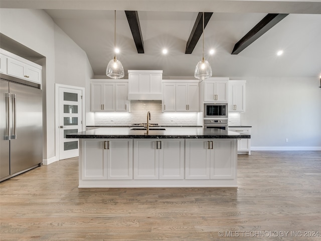 kitchen with backsplash, a center island with sink, built in appliances, beamed ceiling, and white cabinetry