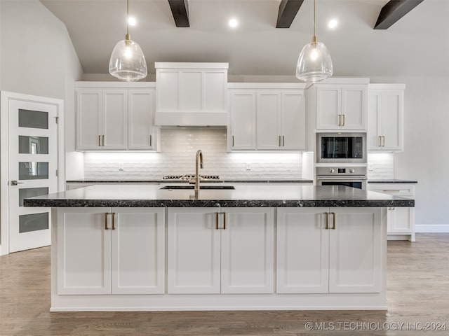 kitchen with black microwave, white cabinetry, stainless steel oven, decorative light fixtures, and a kitchen island with sink