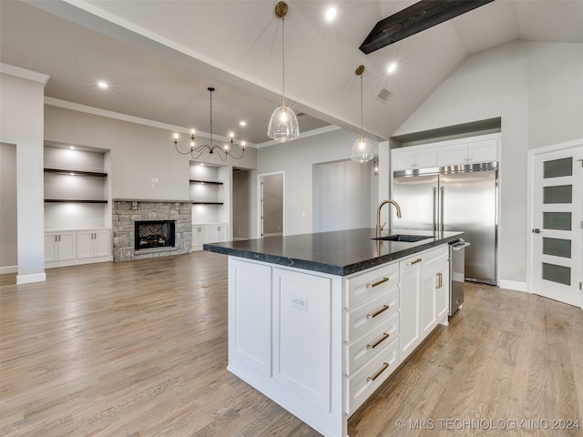 kitchen featuring a center island with sink, sink, built in shelves, a fireplace, and white cabinetry