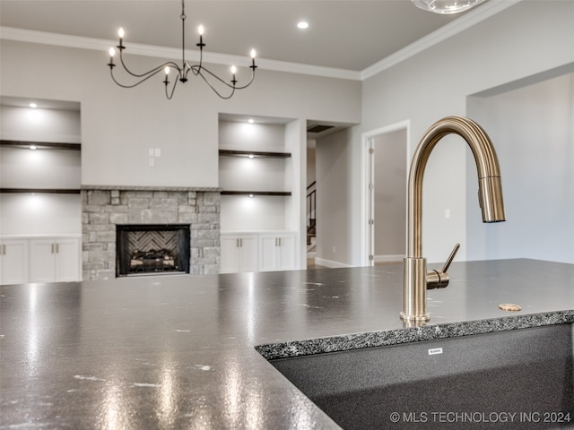 kitchen with built in shelves, sink, a stone fireplace, a notable chandelier, and crown molding