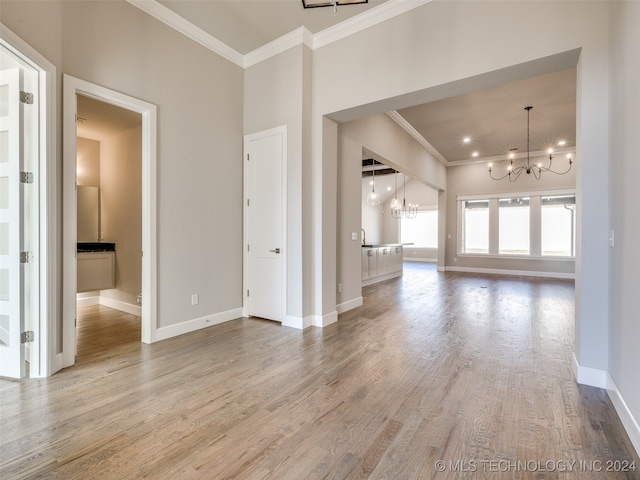 unfurnished living room featuring an inviting chandelier, ornamental molding, and hardwood / wood-style flooring