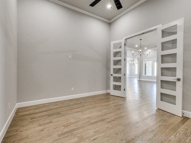 empty room with wood-type flooring, ceiling fan with notable chandelier, and crown molding