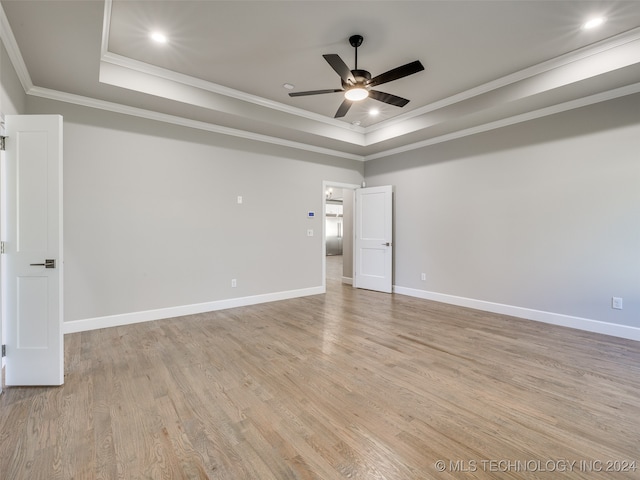 empty room with light wood-type flooring, a raised ceiling, ceiling fan, and crown molding