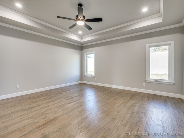 empty room with a raised ceiling, crown molding, light hardwood / wood-style flooring, and ceiling fan