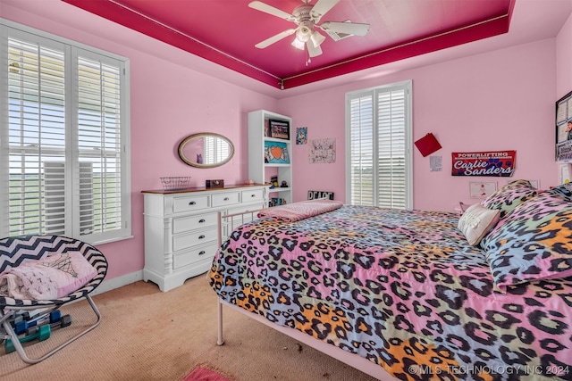 bedroom with a raised ceiling, light colored carpet, and ceiling fan