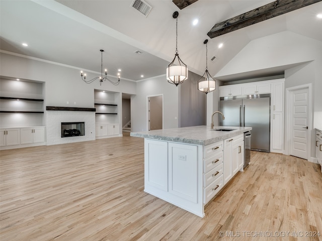 kitchen with light hardwood / wood-style flooring, decorative light fixtures, a kitchen island with sink, a fireplace, and white cabinets