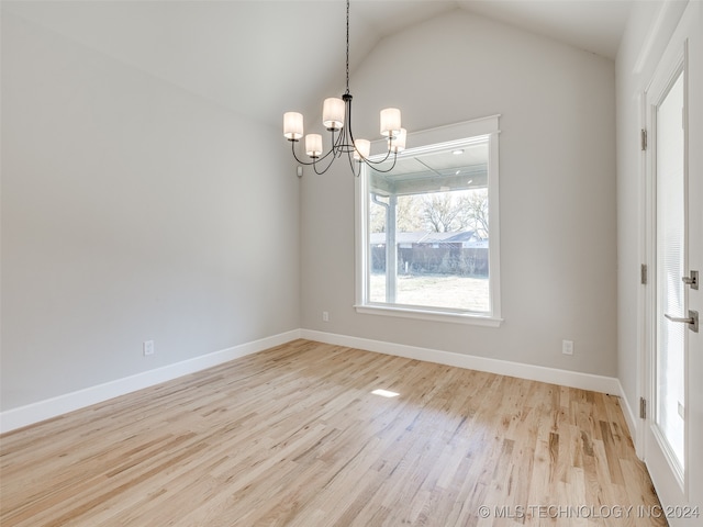 empty room featuring a chandelier, lofted ceiling, and light wood-type flooring