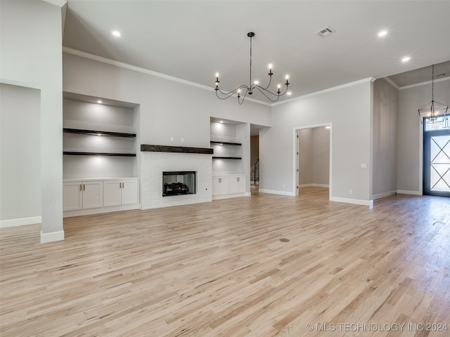 unfurnished living room featuring built in shelves, a chandelier, light hardwood / wood-style floors, and ornamental molding