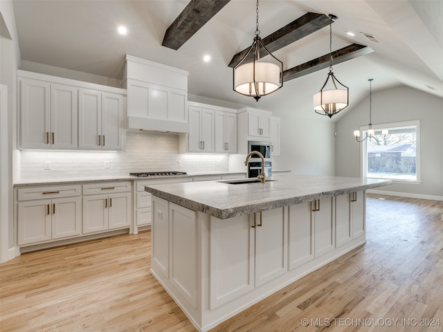 kitchen featuring white cabinets, sink, light hardwood / wood-style flooring, decorative backsplash, and an island with sink