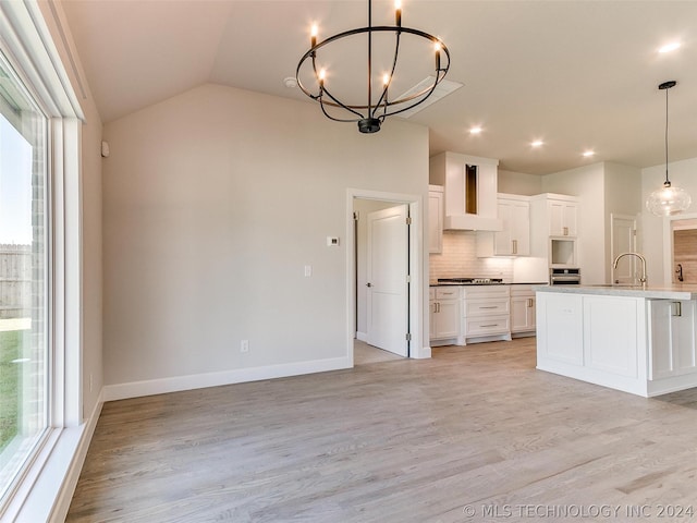 kitchen featuring wall chimney range hood, an inviting chandelier, hanging light fixtures, light hardwood / wood-style floors, and white cabinets