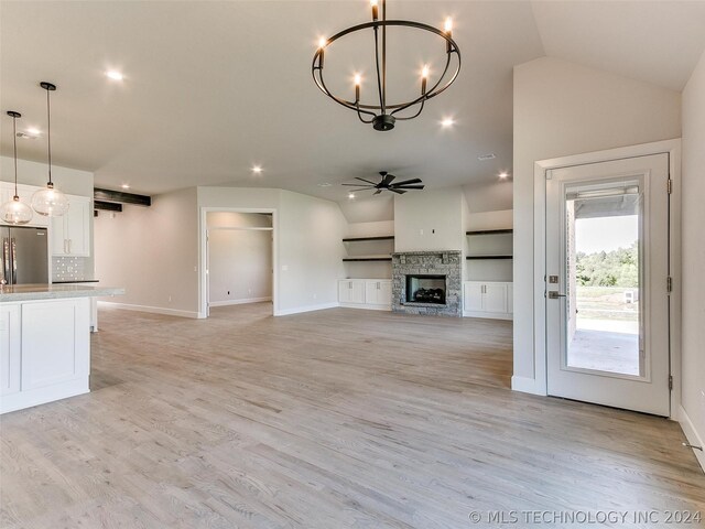 unfurnished living room featuring vaulted ceiling, a stone fireplace, ceiling fan with notable chandelier, and light hardwood / wood-style floors