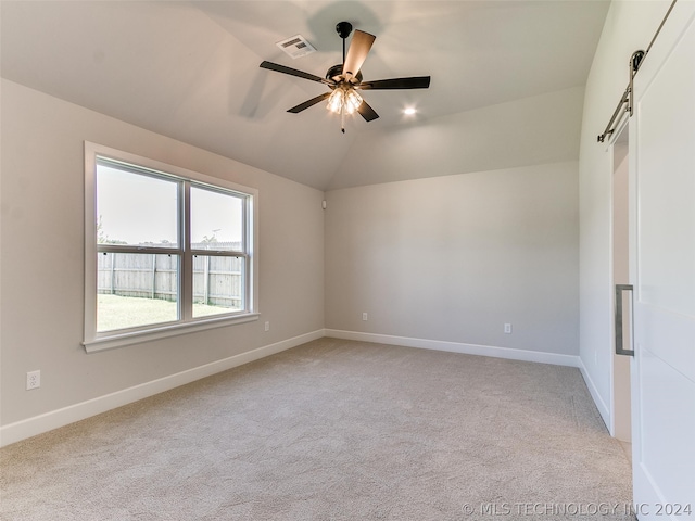 carpeted spare room with a barn door, lofted ceiling, and ceiling fan